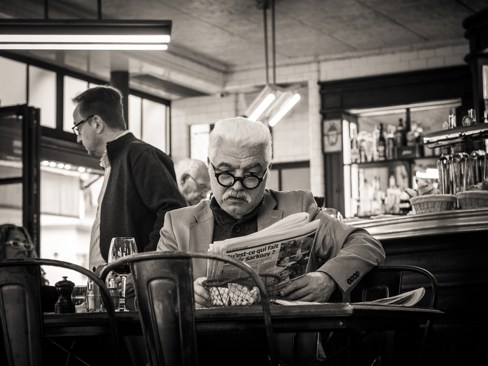 Black and white photograph of a Parisian man reading newspaper in a bistro